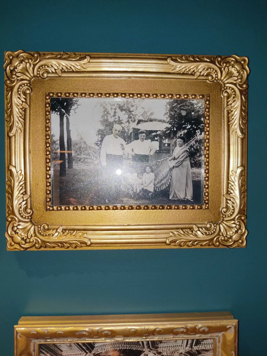 Gold framed black and white photograph of two men, a woman, and 3 children outside in a hammock.