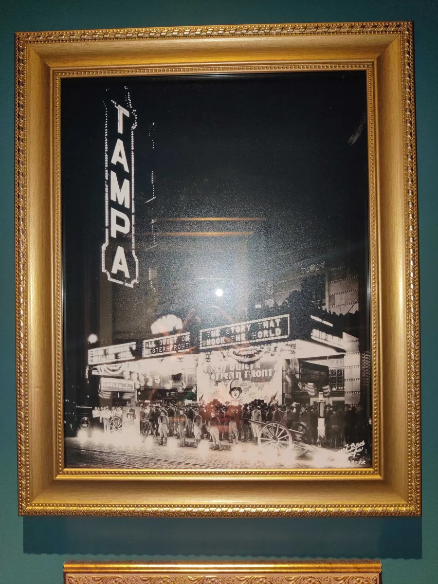 Framed black and white photograph of the Tampa Theatre marquee illuminated at night, surrounded by crowds of people on the street below. The marquee is advertising the 1930 film All Quiet on the Western Front.