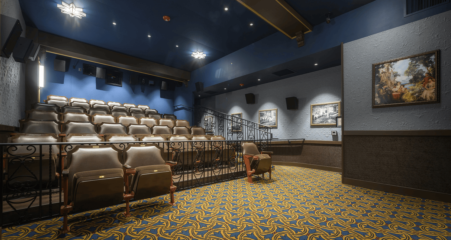 A view of the interior of the John T. Taylor Screening Room from the perspective of the film screen looking out over the empty 43 seat microcinema. Framed historical photos of the Tampa Theatre are lining the entrance ramp walkway.